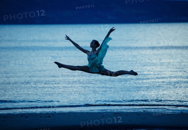 Caucasian ballerina jumping on beach at sunset
