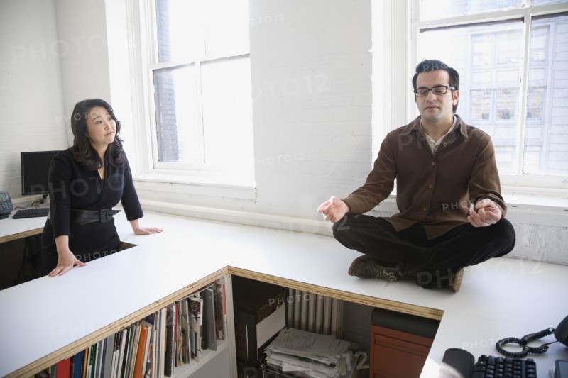 Hispanic businessman meditating next to coworker