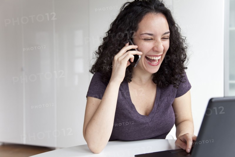 Hispanic woman talking on cell phone and using laptop
