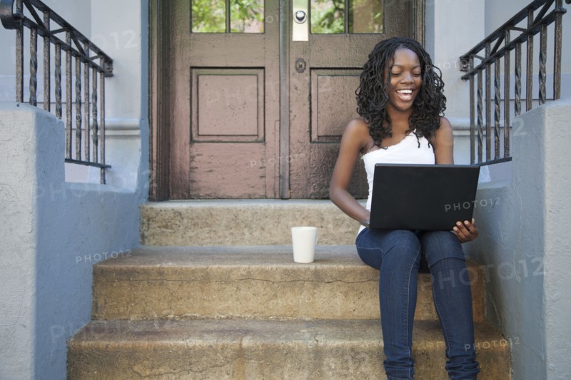 Black woman using laptop on front stoop