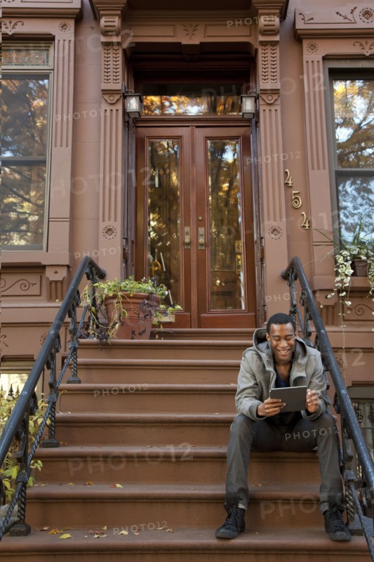 Black man sitting on front stoop using digital tablet