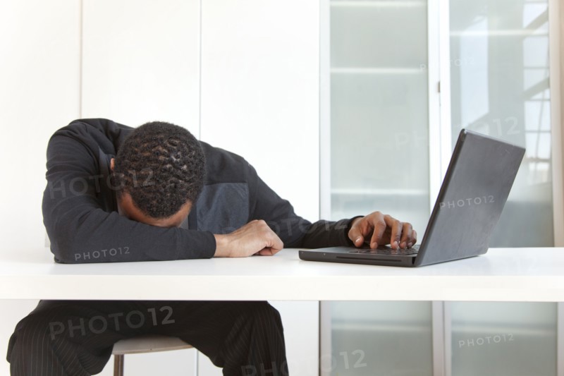 Tired Black businessman sleeping near laptop