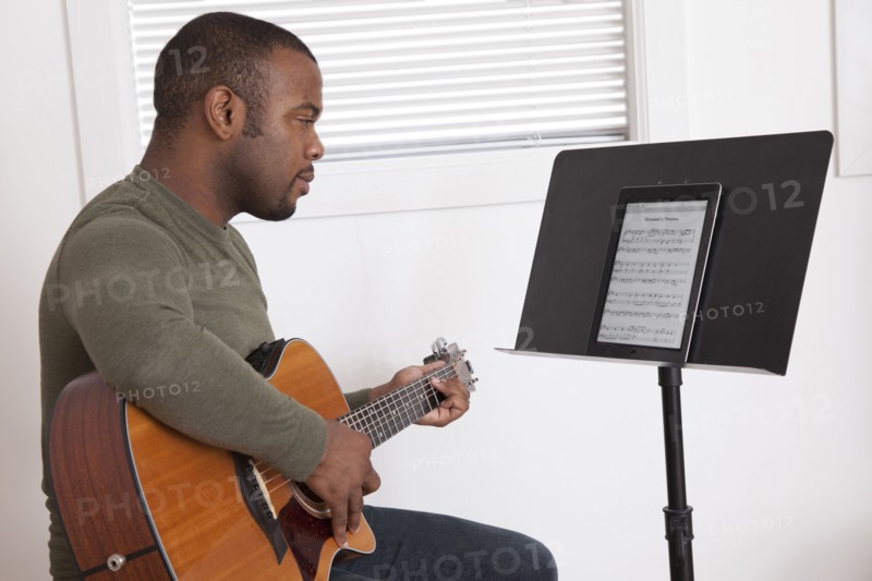 Black man practicing guitar with digital tablet