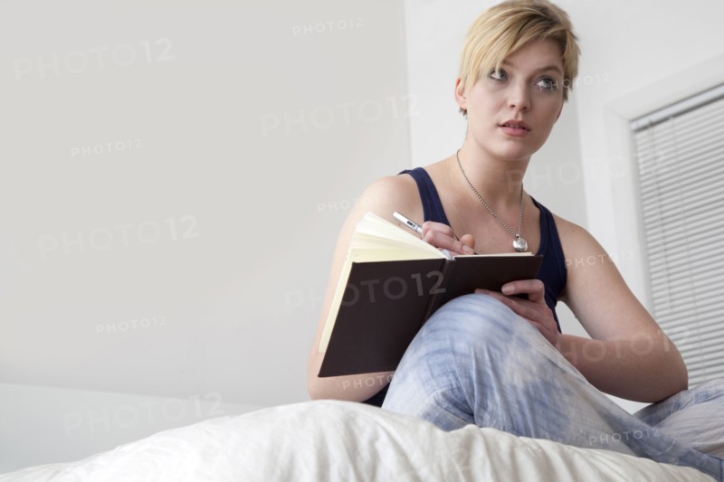 Caucasian woman writing in diary on bed