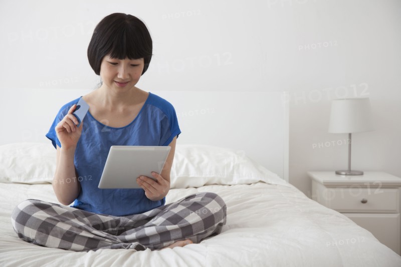 Chinese woman using tablet computer on bed