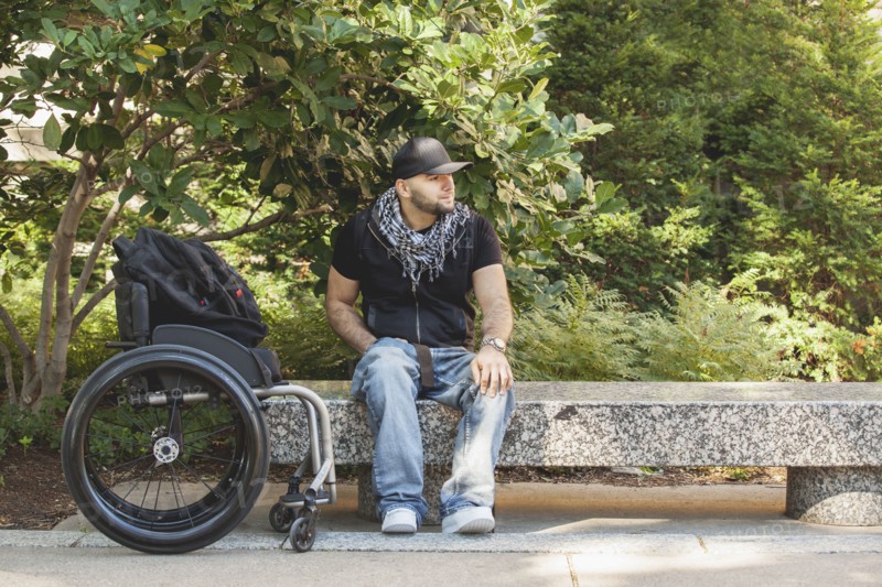 Disabled man and wheelchair sitting on stone bench