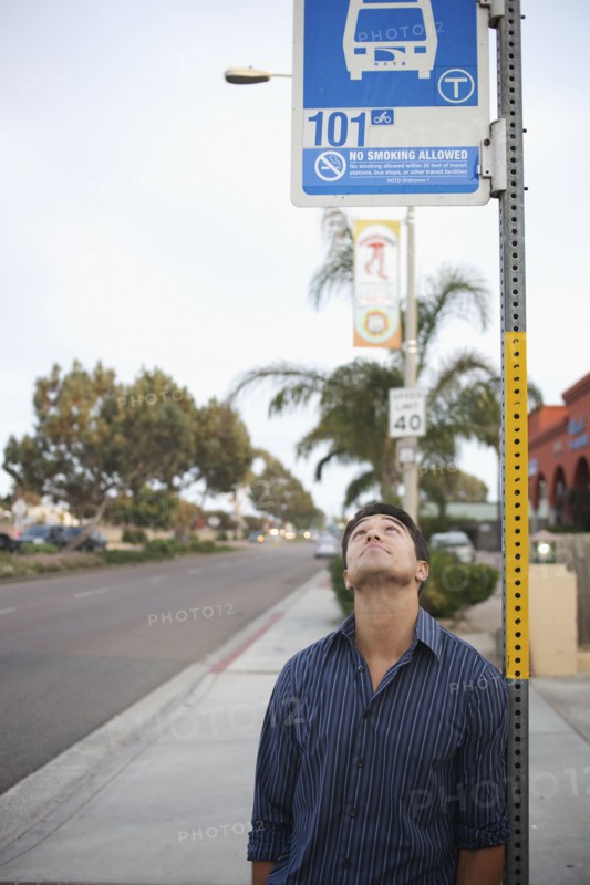 Mixed race man looking at bus stop sign
