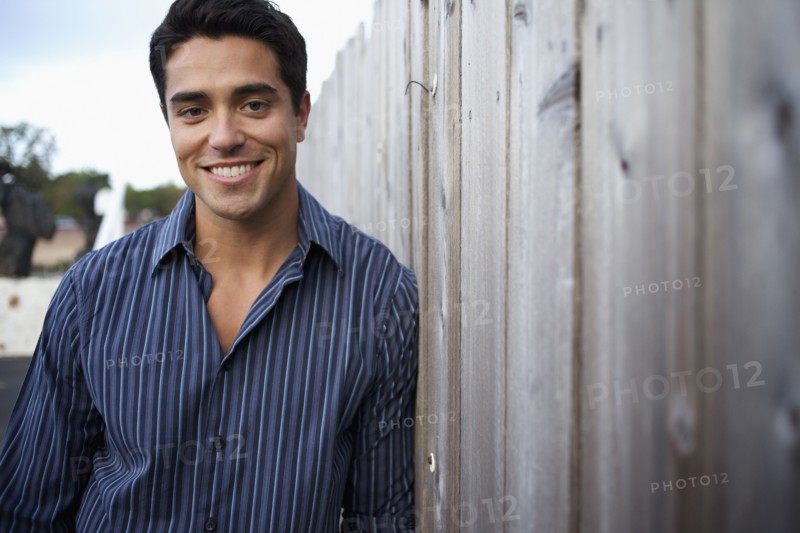 Mixed race man leaning against fence