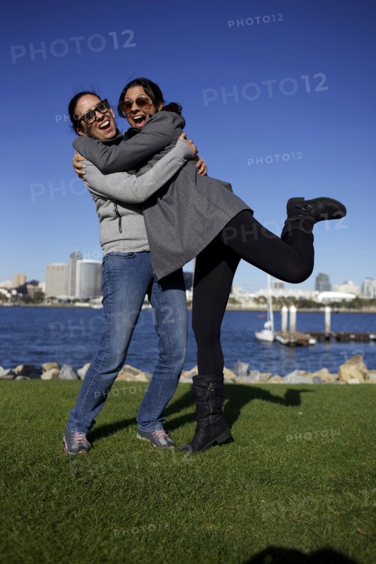 Grinning mixed race sisters hugging outdoors
