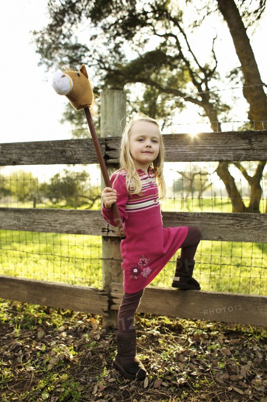 Caucasian girl holding stick horse near fence