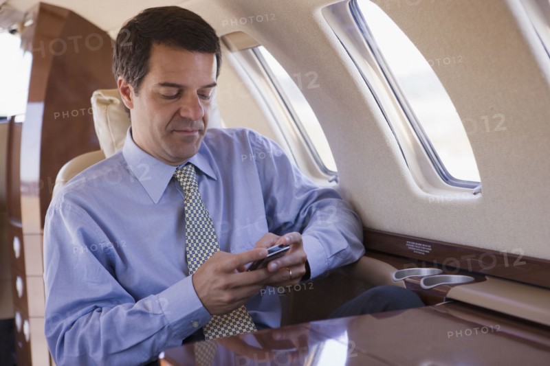 Hispanic businessman using cell phone on airplane