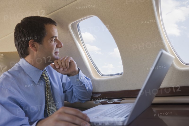 Hispanic businessman with laptop looking out airplane window