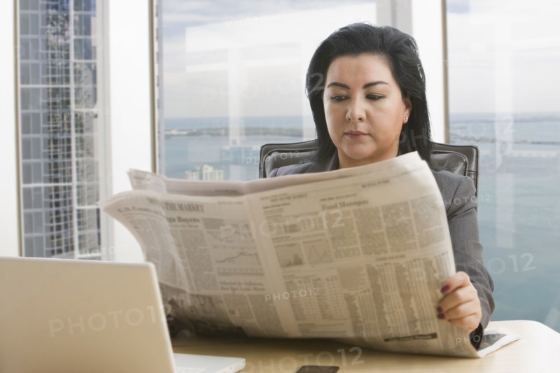 Hispanic businesswoman reading newspaper in office