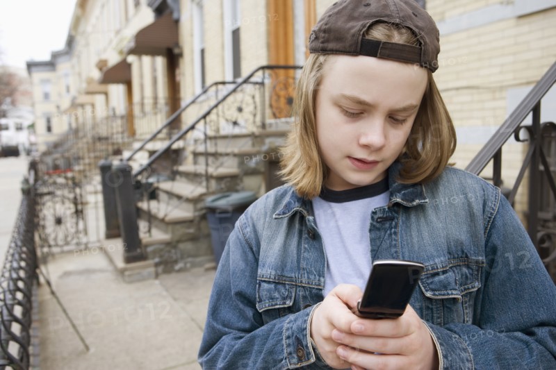 Caucasian boy text messaging on cell phone on sidewalk