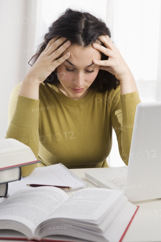 Mixed race woman with headache studying textbooks