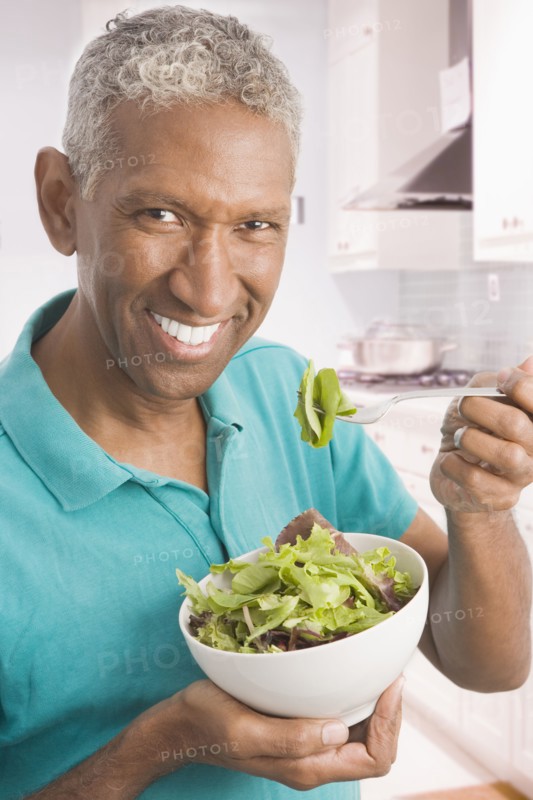 Mixed race man eating salad in kitchen