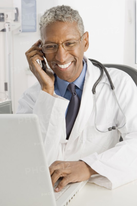 Mixed race doctor sitting at desk talking on cell phone
