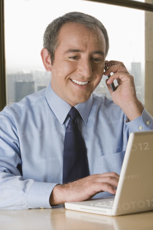 Hispanic businessman with laptop talking on cell phone