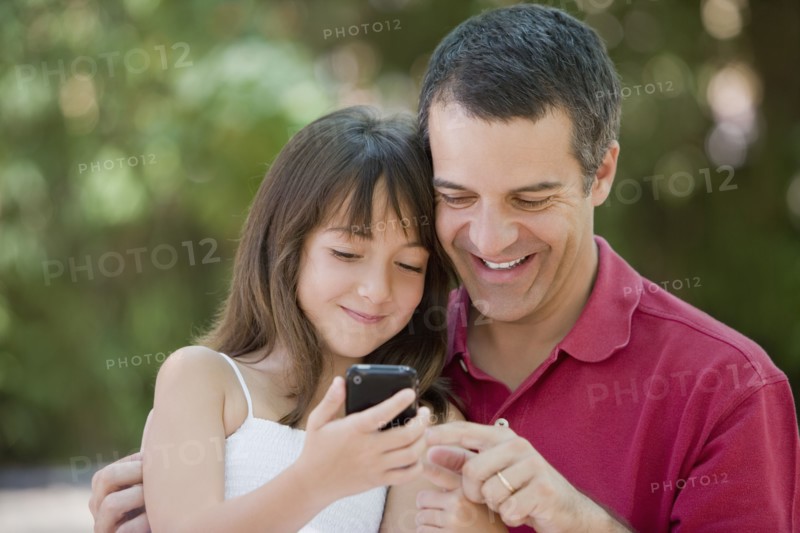 Hispanic father and daughter text messaging on cell phone