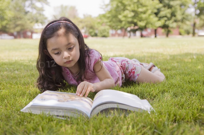 Hispanic girl laying in grass reading book