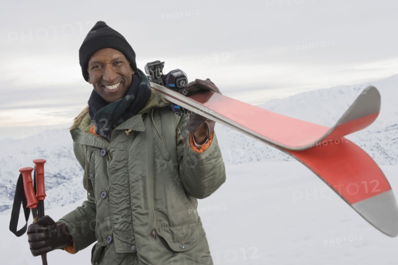 Mixed race man carrying skis on snowy slope