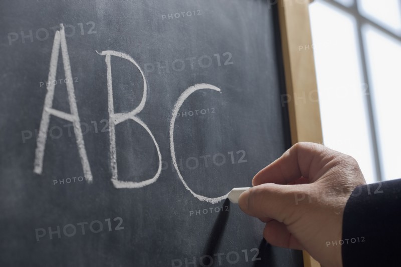 Hispanic teacher writing 'ABC' on chalkboard