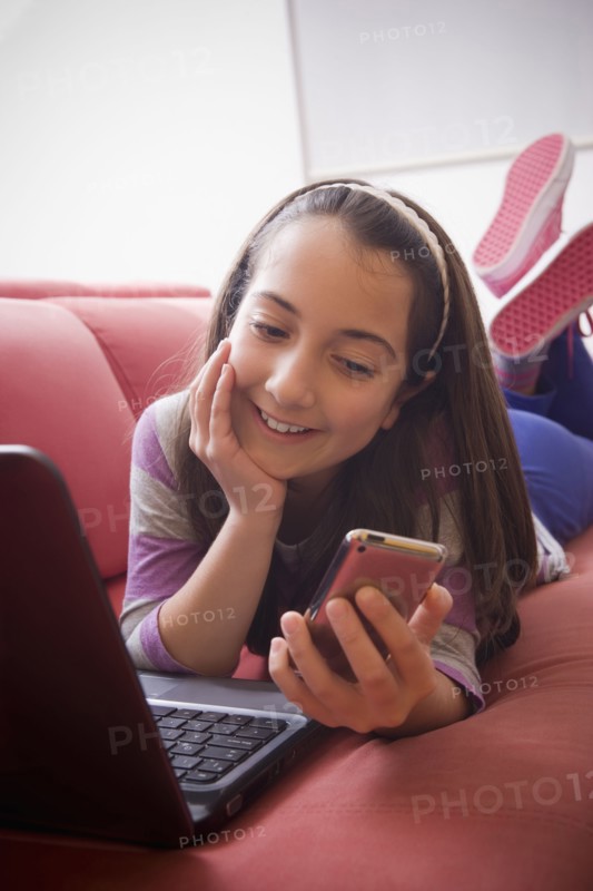 Hispanic girl using laptop and cell phone on sofa