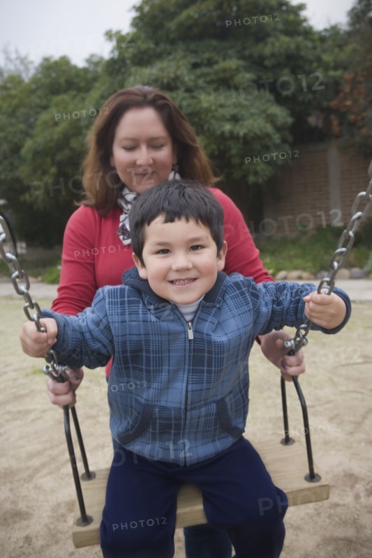 Hispanic mother pushing son on swings