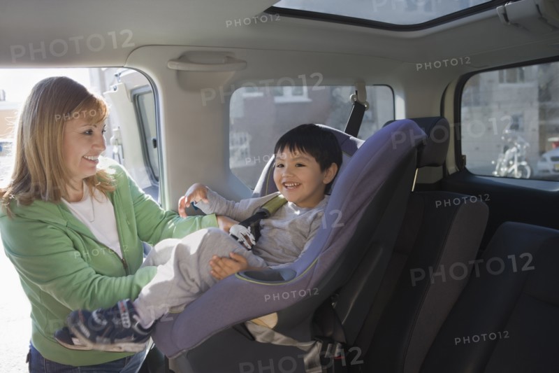 Hispanic woman loading son into car seat