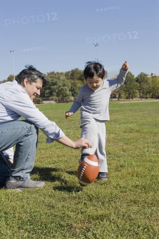 Hispanic father and son playing football outdoors