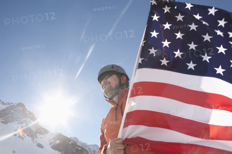Hispanic hiker planting American flag on snowy mountain