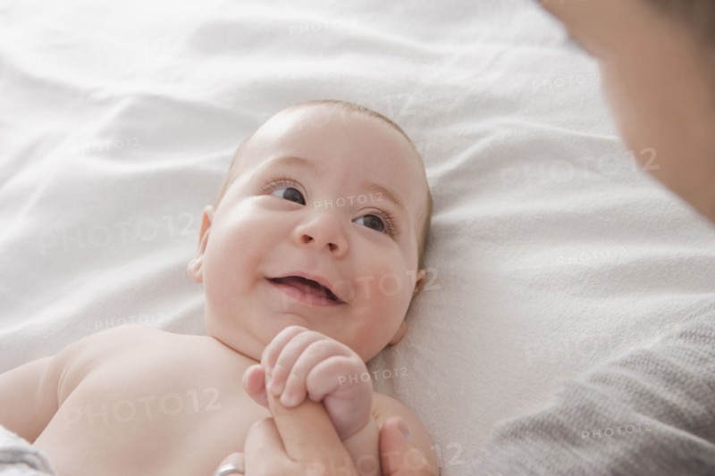 Father admiring Hispanic baby boy on bed