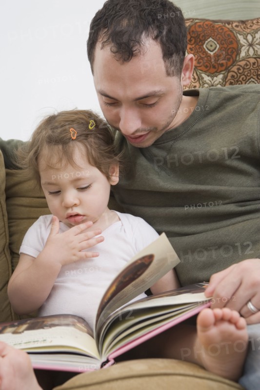 Hispanic father reading to daughter on sofa