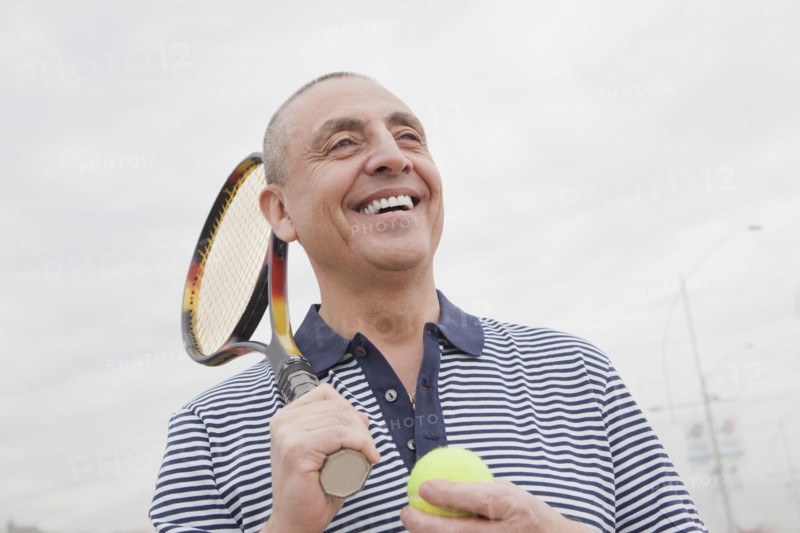 Hispanic senior man carrying tennis racket and ball