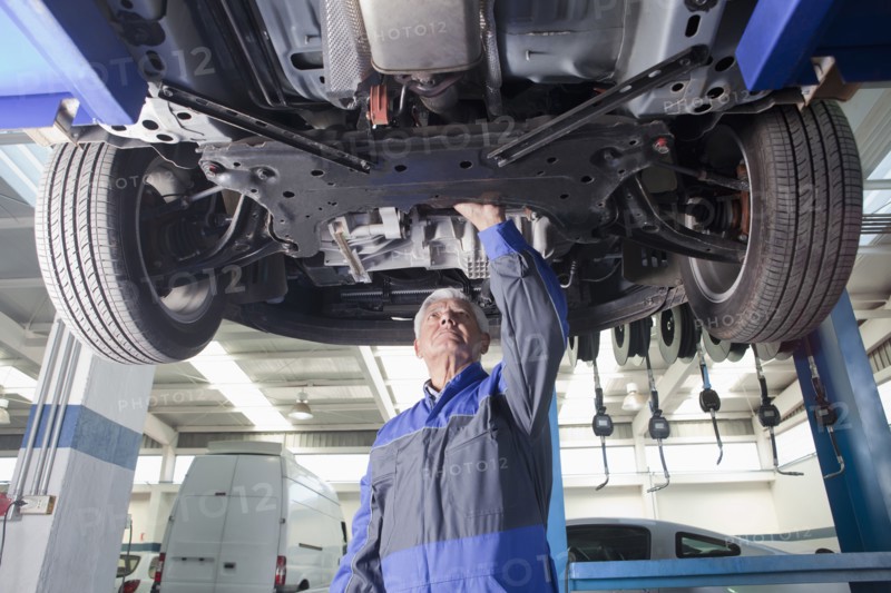 Older Hispanic mechanic repairing car in garage