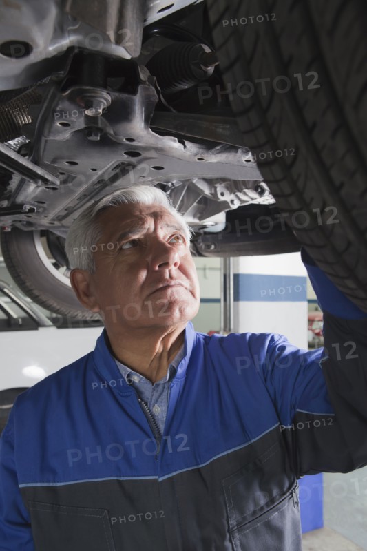 Older Hispanic mechanic repairing car in garage