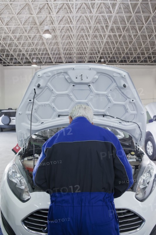 Older Hispanic mechanic repairing car in garage