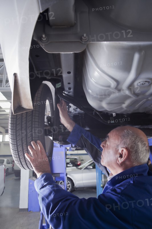 Older Hispanic mechanic repairing car wheel in garage