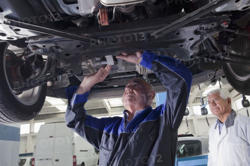 Older Hispanic mechanic repairing car in garage