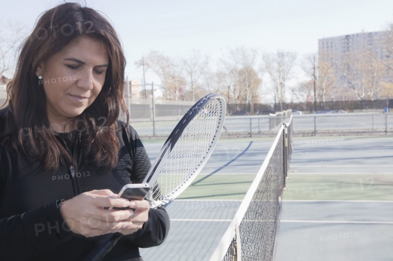 Hispanic woman using cell phone on tennis court