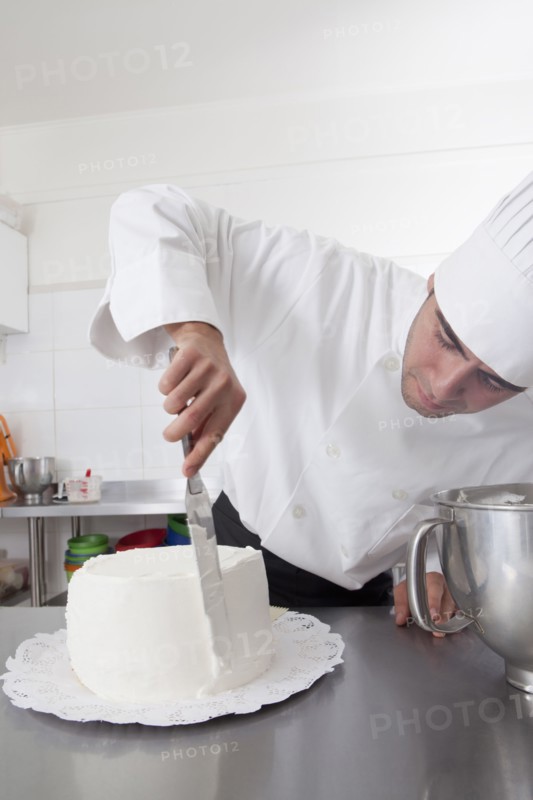 Hispanic chef spreading icing on side of cake