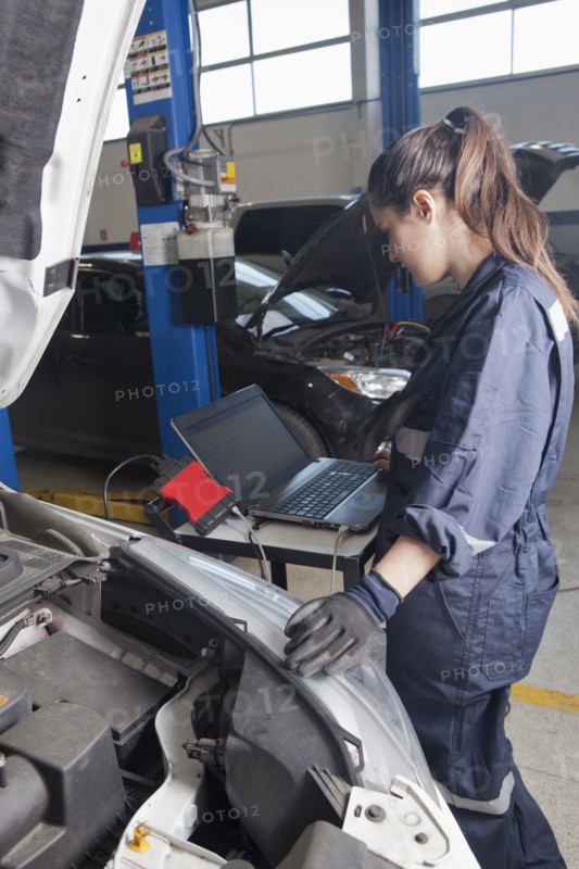 Hispanic mechanic diagnosing car engine with laptop