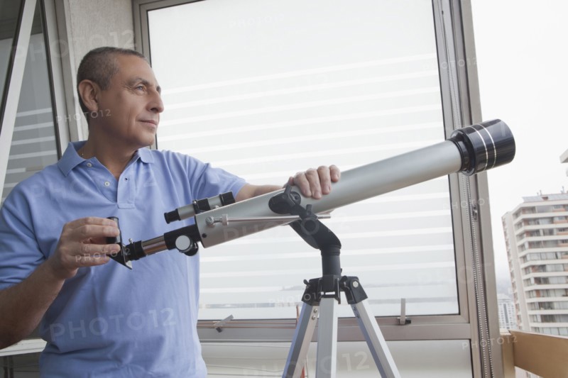 Hispanic man holding telescope near window