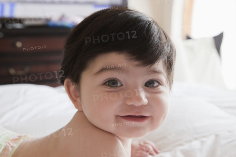 Portrait of smiling Hispanic baby boy laying on bed