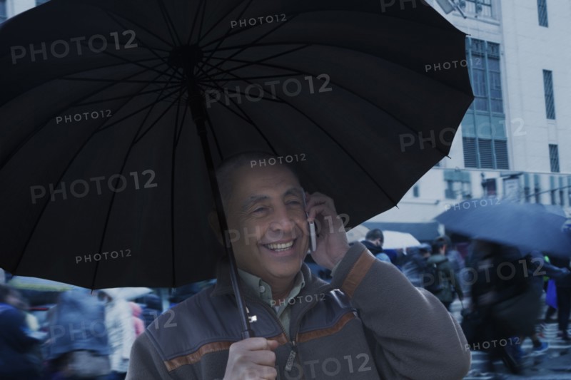 Smiling Hispanic man holding umbrella and talking on cell phone