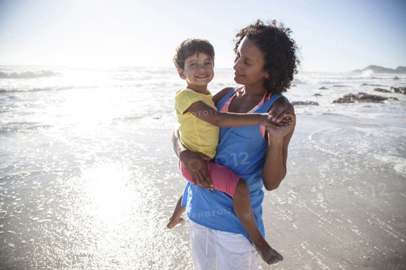 Mixed race mother carrying daughter on beach