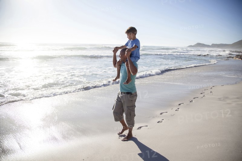 Mixed race father carrying son on shoulders on beach