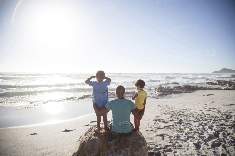 Mixed race father and children sitting on beach