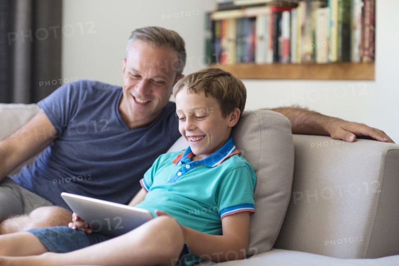 Caucasian father and son using digital tablet on sofa
