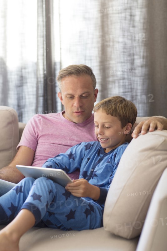 Caucasian father and son using digital tablet on sofa